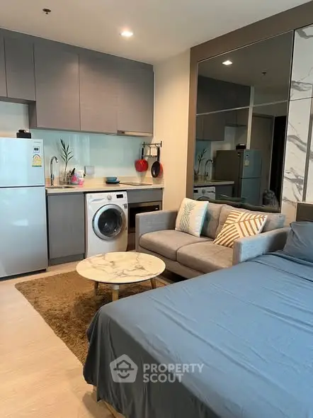 Modern studio apartment with stylish kitchen and cozy living area, featuring a washing machine and sleek decor.