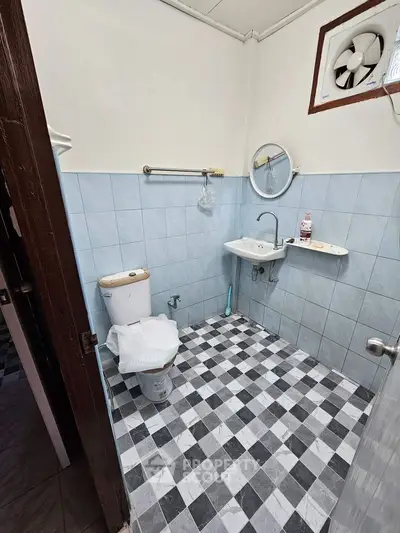 Compact bathroom with checkered floor tiles, wall-mounted sink, and classic white toilet, complemented by a small window for natural light.