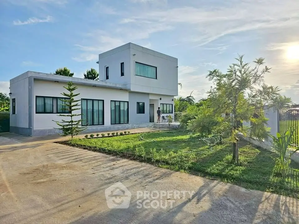 Modern two-story house with spacious garden and driveway under clear sky.