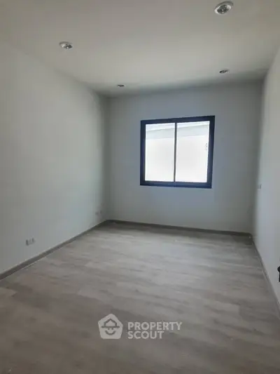 Spacious empty room with large window and modern flooring, ideal for customization.