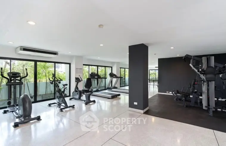 Spacious modern gym with large windows and state-of-the-art equipment in a luxury building.