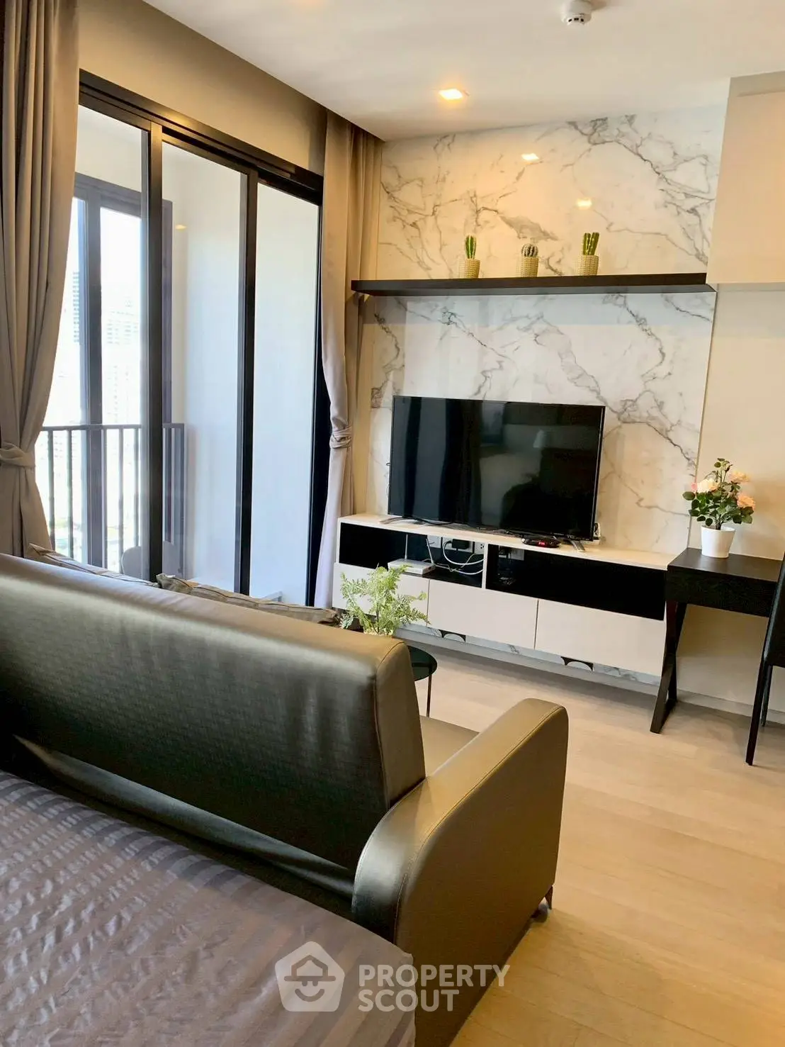 Modern living room with sleek furniture and marble accent wall, featuring a large TV and balcony access.