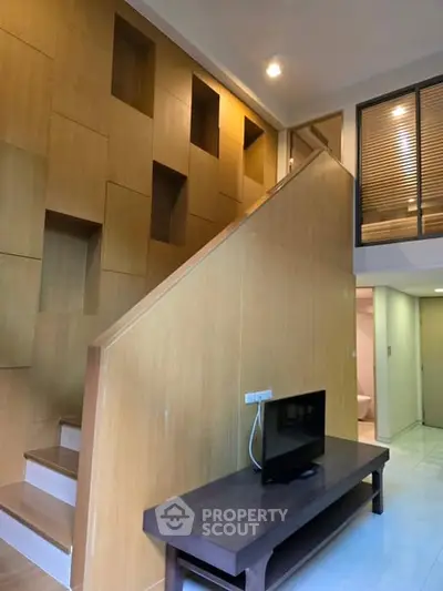 Modern duplex interior with wooden staircase and sleek TV setup