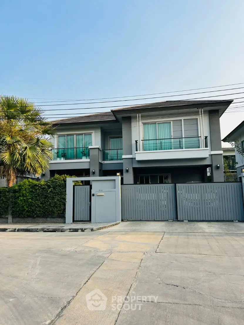 Modern two-story house with sleek design and gated entrance, featuring large windows and a lush palm tree.