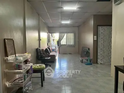 Spacious living room with tiled flooring and natural light, featuring comfortable seating and a fan.