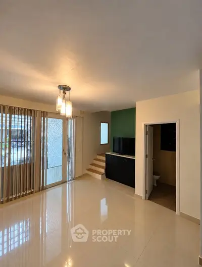 Spacious living room with modern lighting and glossy tile flooring, featuring a step-up design and large windows.
