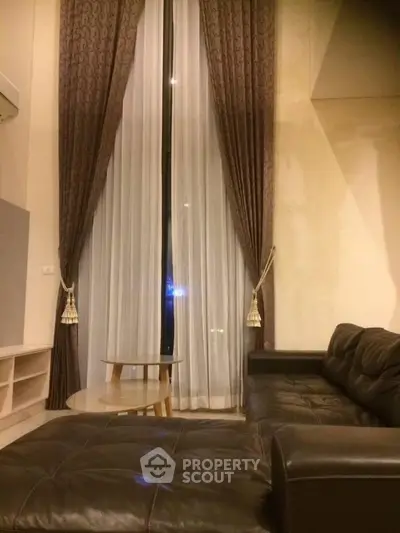 Luxurious living room with high ceilings and elegant curtains, featuring a stylish leather sofa and modern coffee table.