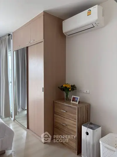 Modern bedroom with sleek wardrobe and air conditioning, featuring stylish wooden furniture and bright decor.