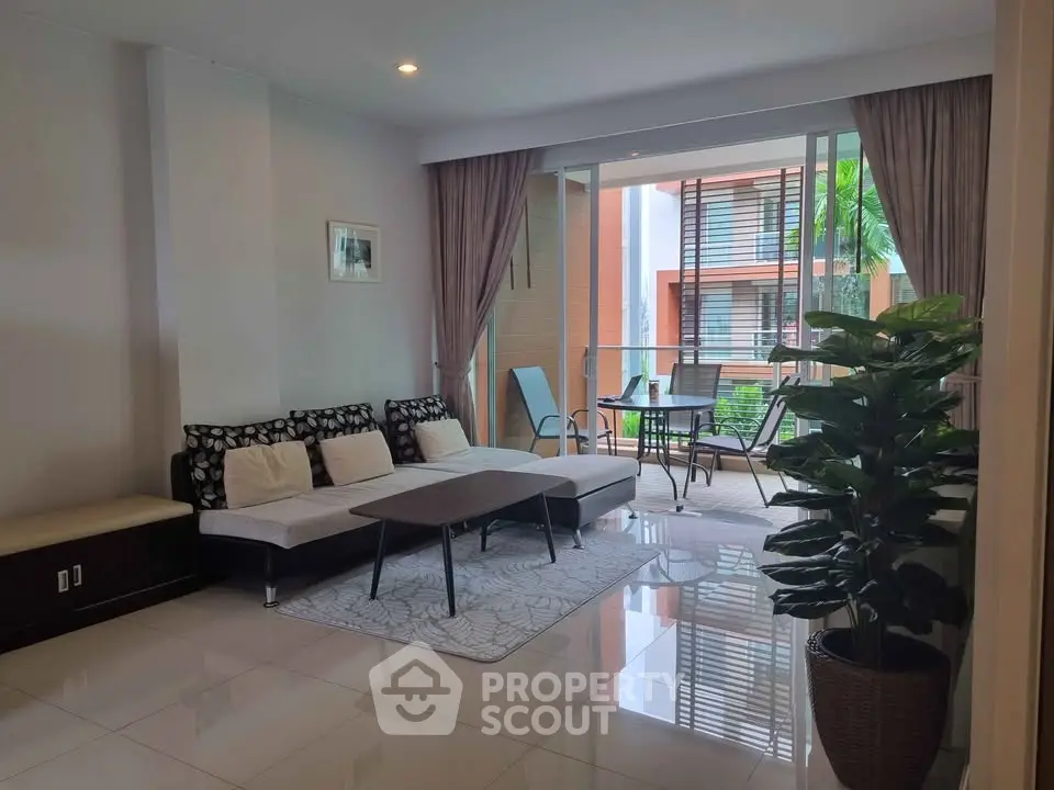 Modern living room with large windows and balcony access, featuring stylish furniture and lush greenery.