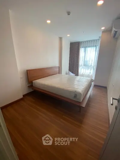 Spacious bedroom with wooden flooring and large window for natural light