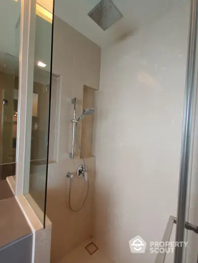 Modern bathroom with a spacious walk-in shower featuring a large overhead rain showerhead and a handheld sprayer, enclosed by clear glass doors.