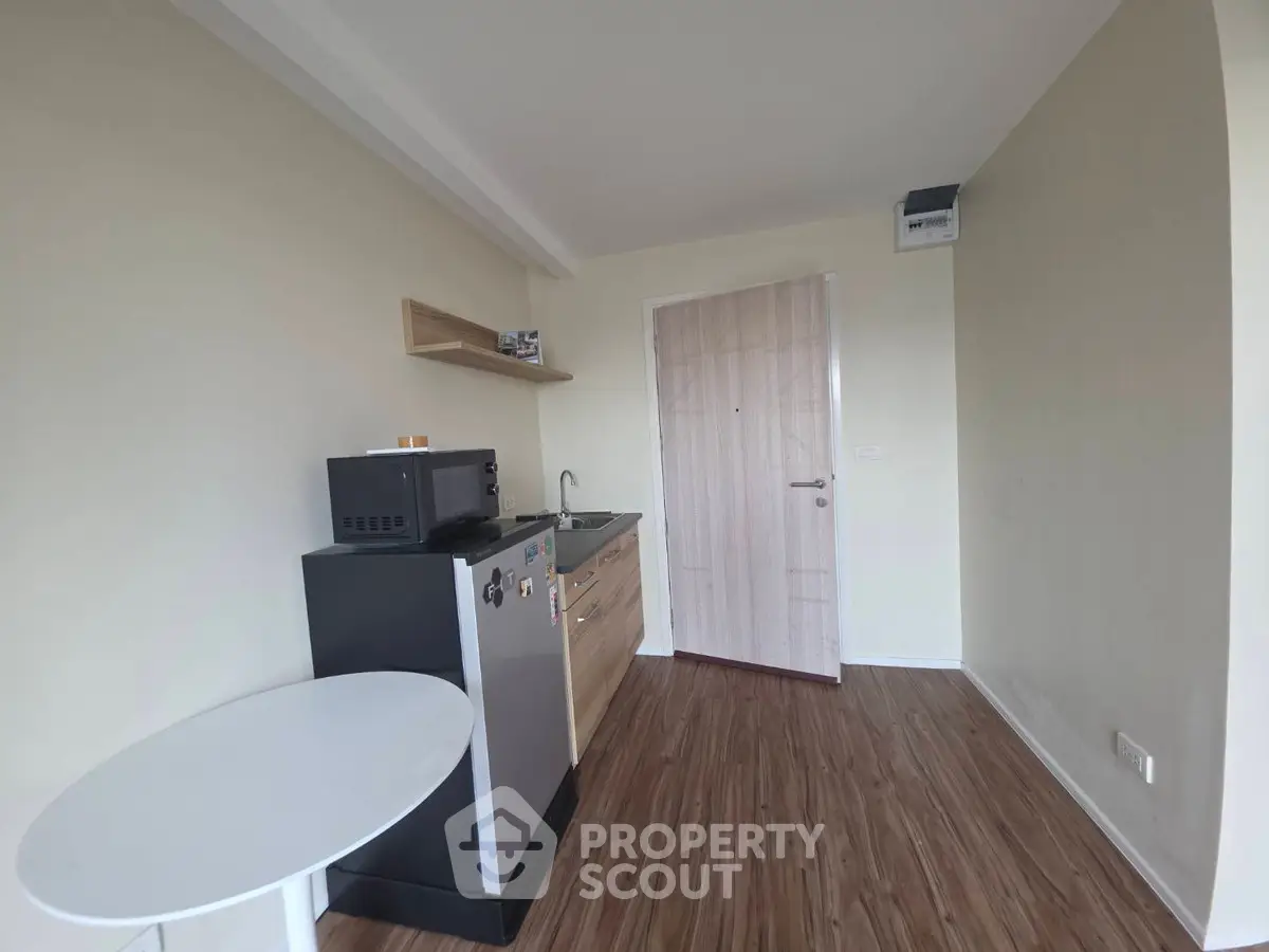 Compact kitchenette with modern appliances and wooden flooring in a cozy apartment.