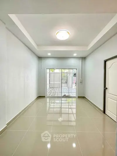 Spacious interior with glossy tiled floors and modern lighting, leading to a bright outdoor area.