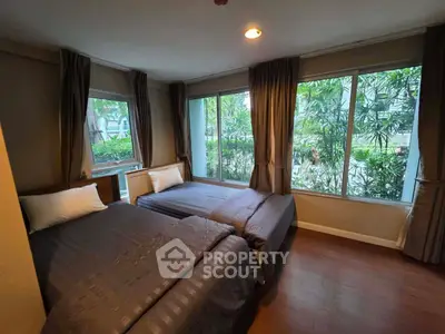Spacious bedroom with twin beds and large windows overlooking lush greenery.