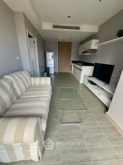 Modern living room with striped sofa, glass coffee table, and sleek kitchen area in open layout.