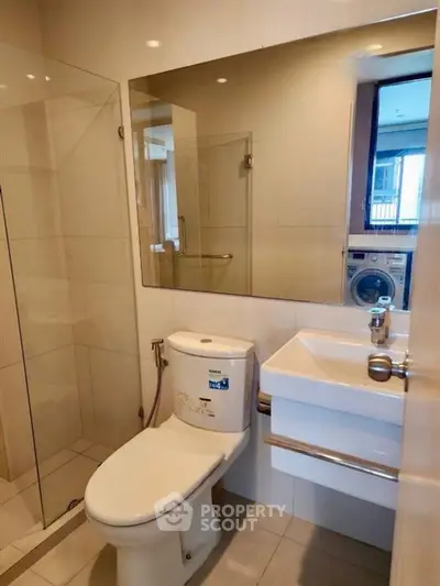Modern bathroom with glass shower and washing machine in sleek apartment.