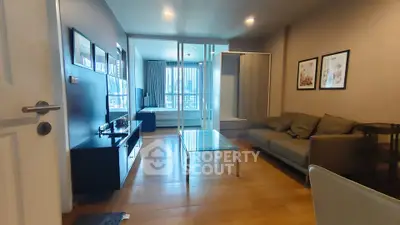 Modern living room with glass coffee table and cozy sofa, featuring a view into the bedroom.