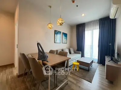 Modern living room with stylish dining area and cozy seating, featuring elegant lighting and natural light from large window.