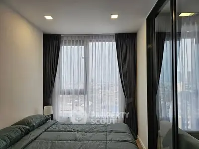 Modern bedroom with large windows and city view, featuring elegant curtains and cozy bedding.
