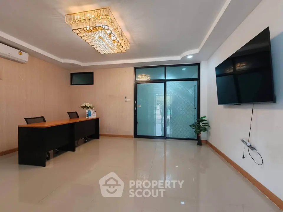 Modern office space with elegant chandelier and large TV screen, ideal for professional meetings.