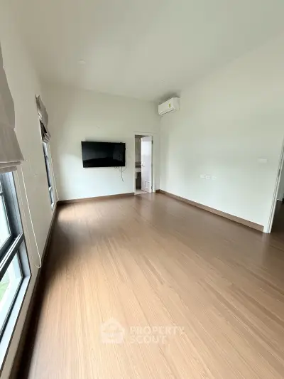 Spacious empty room with wooden flooring and wall-mounted TV, ideal for customization.