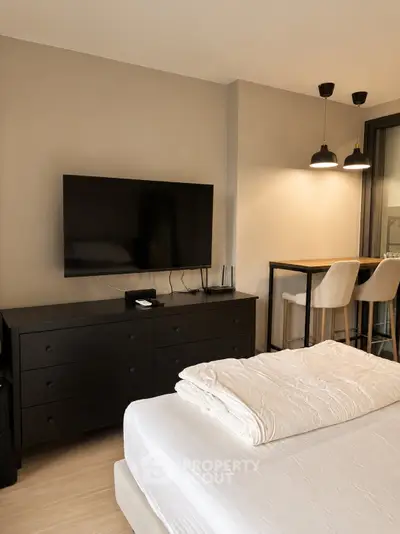 Modern bedroom with TV and stylish lighting, featuring a cozy bed and sleek dresser.