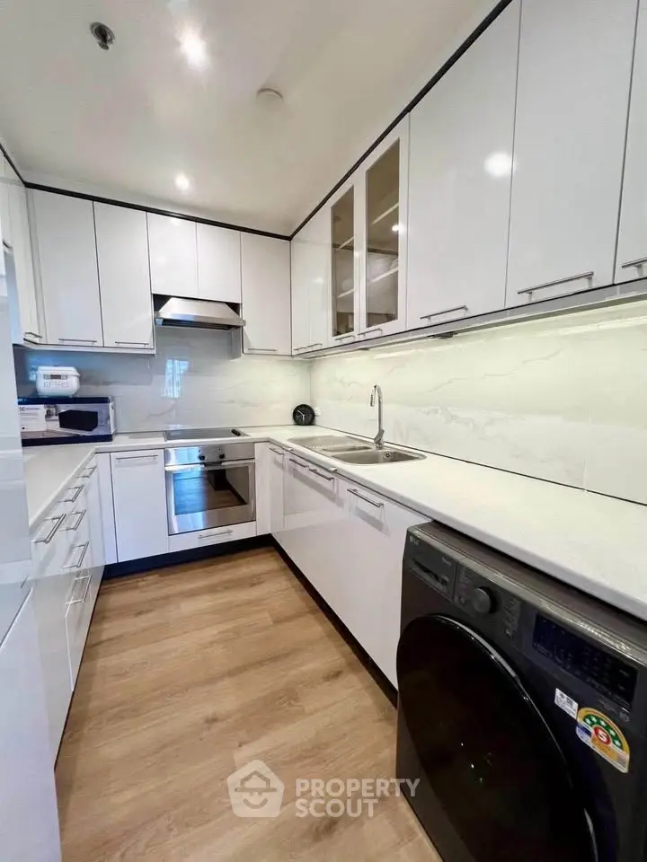 Modern kitchen with sleek white cabinets, built-in appliances, and wood flooring