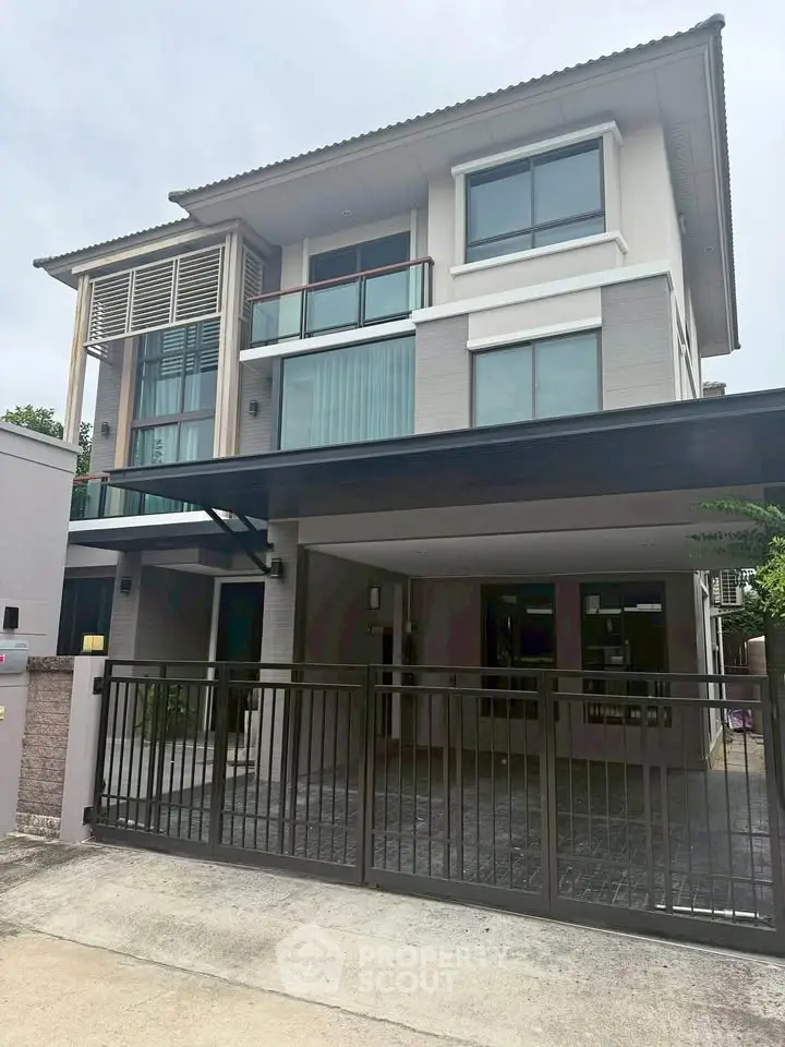 Modern three-story house with large windows and gated entrance in a suburban neighborhood.