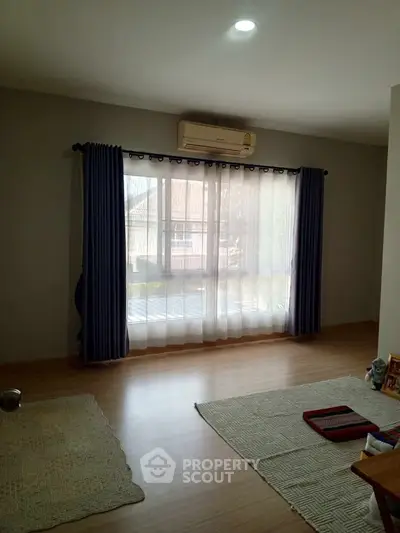 Spacious living room with large window and wooden flooring, perfect for natural light and comfort.