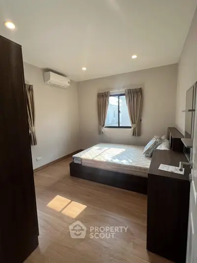 Cozy bedroom with wooden flooring and natural light, featuring a modern air conditioning unit.