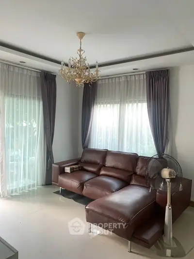 Elegant living room with leather sofa and chandelier, featuring large windows and stylish curtains.