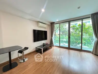 Spacious living room with large windows and garden view, featuring modern decor and wooden flooring.