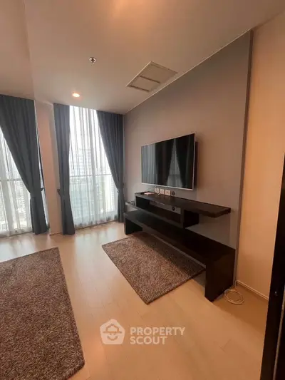Modern living room with sleek TV setup and large windows offering city views.