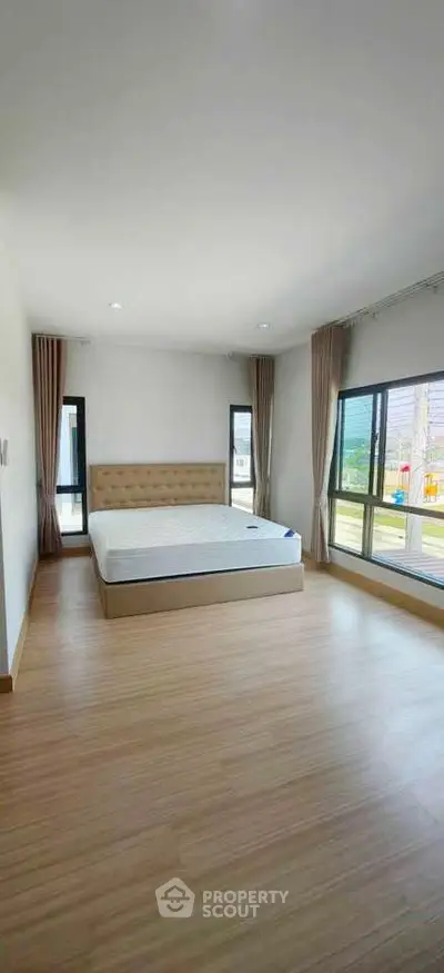 Spacious bedroom with large windows and natural light, featuring a modern bed and wooden flooring.