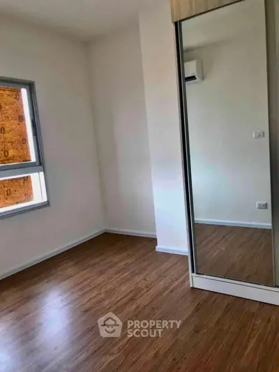 Spacious bedroom with wooden flooring and mirrored wardrobe in modern apartment.