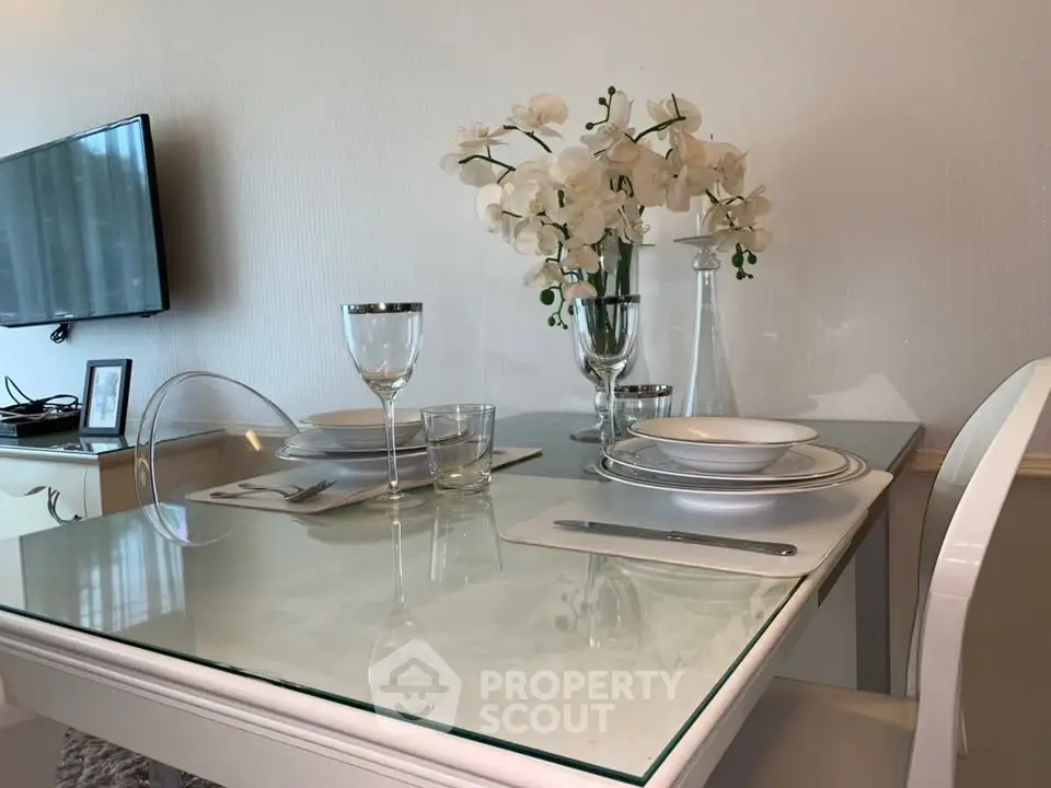 Elegant dining area with glass table, modern decor, and wall-mounted TV in a stylish apartment.
