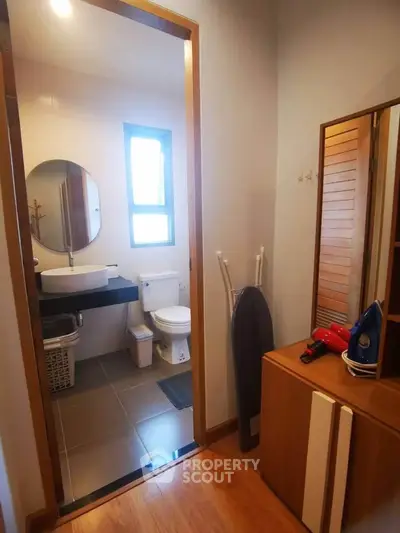 Cozy bathroom with modern fixtures and wooden accents, featuring a round mirror and ample natural light.