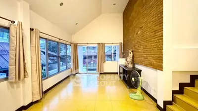 Spacious living room with high ceiling and large windows offering natural light and outdoor view.