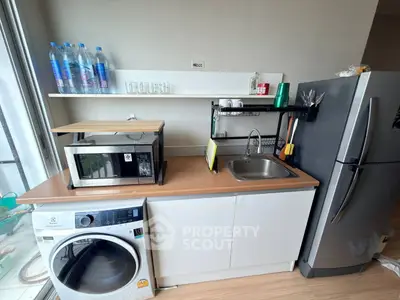 Modern kitchen with washing machine, microwave, and fridge in compact layout.