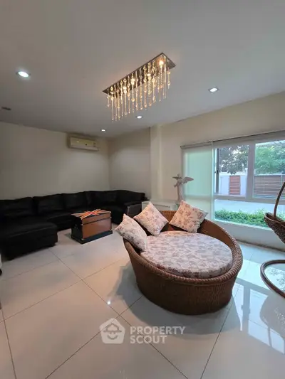 Spacious living room with elegant chandelier and cozy seating, featuring large windows for natural light.