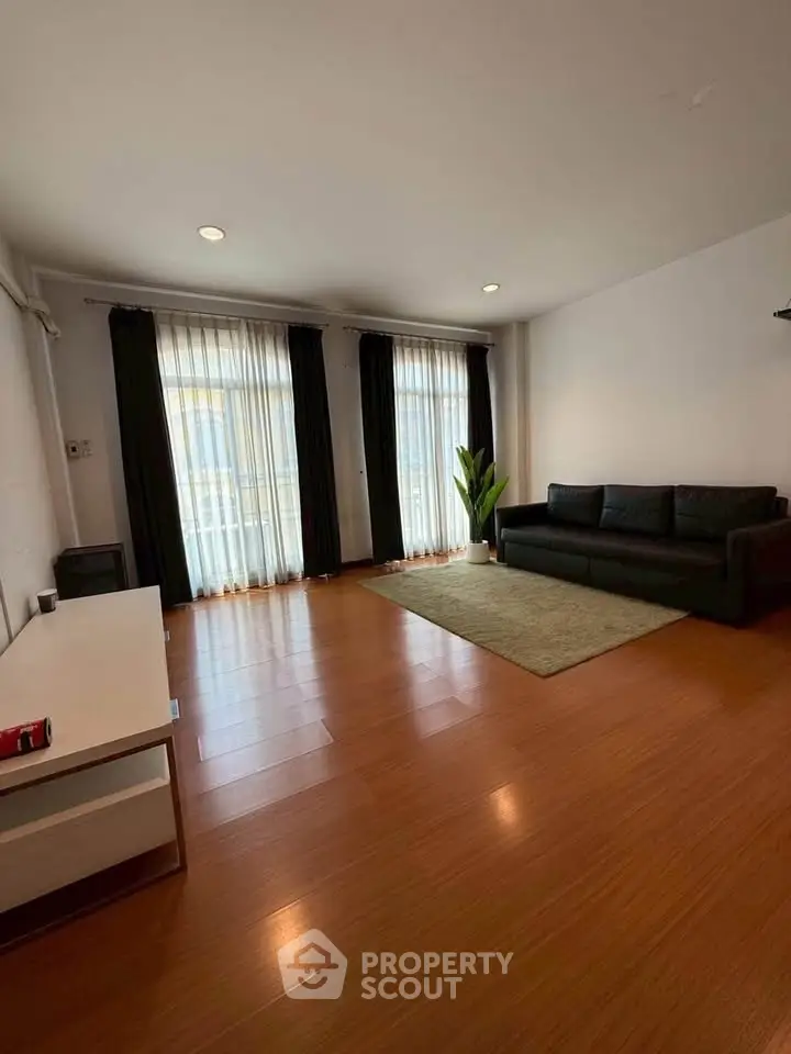 Spacious living room with hardwood floors, large windows, and modern furnishings in a stylish apartment.