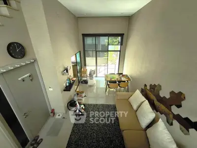 Modern living room with high ceiling and large windows, featuring stylish decor and a cozy seating area.