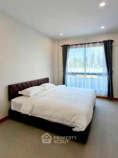 Spacious bedroom with large window and elegant curtains in modern apartment.