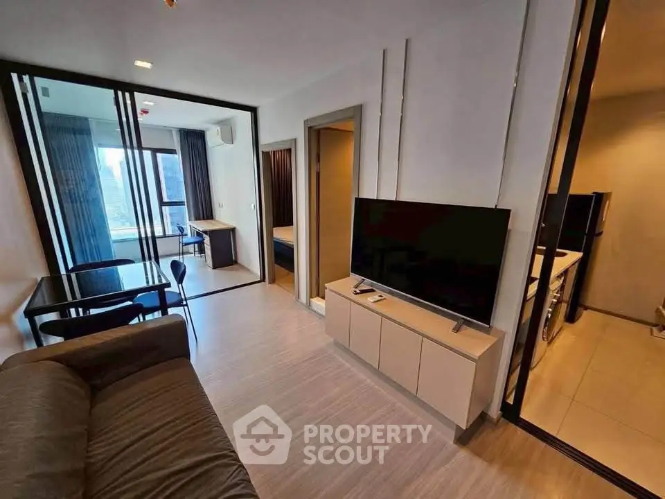Modern living room with sleek furniture and large TV, open layout leading to bedroom with city view.