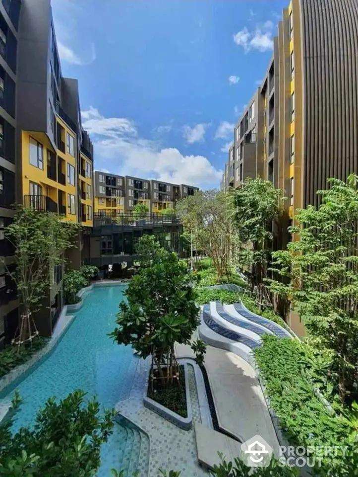 Modern apartment complex with lush garden and swimming pool under a clear blue sky.