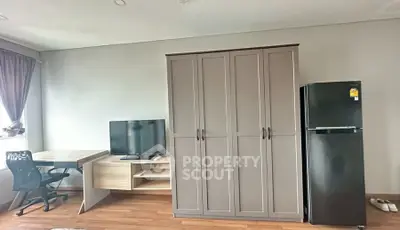 Modern studio apartment with wardrobe, desk, and fridge in bright interior.