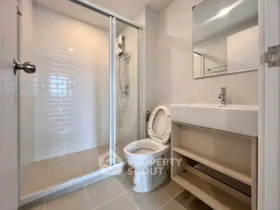 Modern bathroom with glass shower, sleek sink, and toilet in a contemporary apartment.