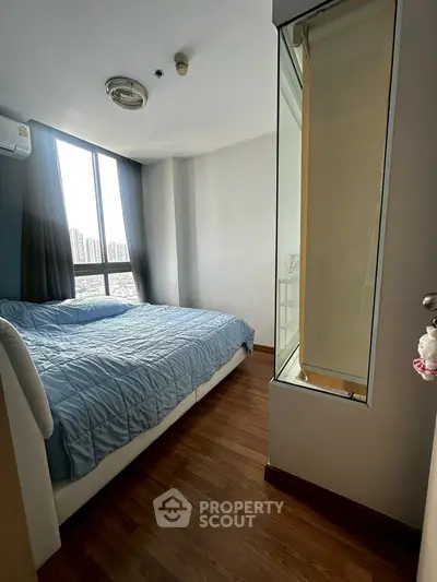 Cozy bedroom with large window offering city views, featuring a comfortable bed and wooden flooring.
