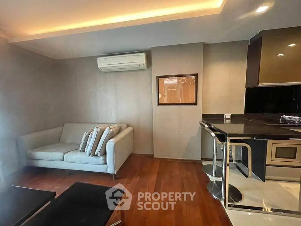 Modern living room with sleek design and cozy sofa, featuring stylish kitchen area with bar seating.