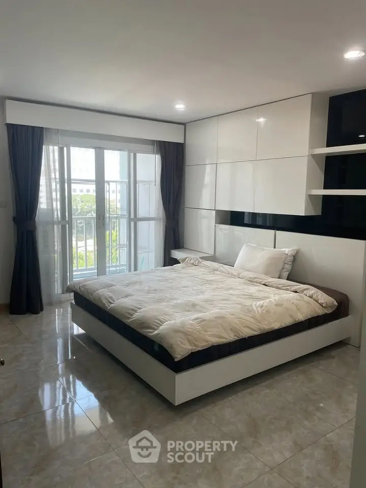 Modern bedroom with large windows and sleek white cabinetry, offering a bright and inviting space.